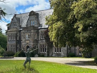 Historic stone mansion with a statue in front and large trees.