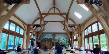People practicing yoga in a wooden hall with large windows.