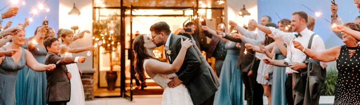 A newly married couple kisses while guests hold sparklers in a celebratory exit.