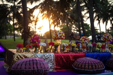 Vibrant floral arrangement on glittery tables with cushions at sunset outdoors.