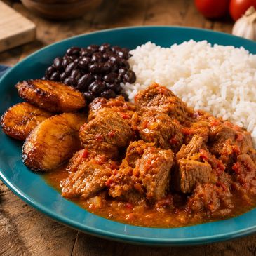 Plate with rice, black beans, fried plantains, and spicy stewed meat.