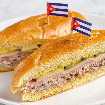 Cuban sandwiches with ham, cheese, pickles, and roast pork, topped with Cuban flag toothpicks.