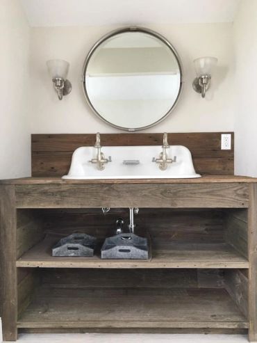 Rustic wooden bathroom vanity with round mirror and dual faucets.