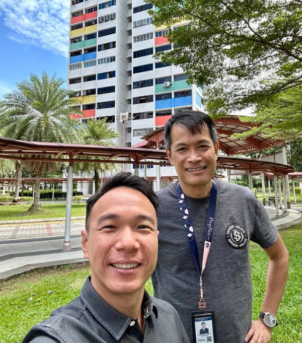 Two men smiling outdoors with colorful building in background.