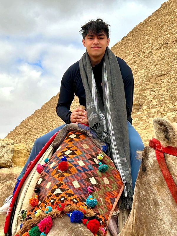 Man riding camel in front of pyramid.