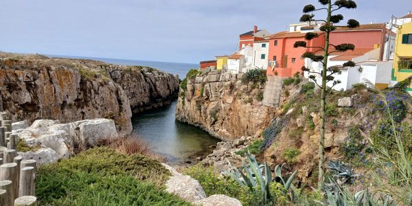 Colorful houses perched on cliffs by a narrow sea inlet under a clear sky.