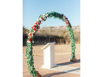 A floral arch with a podium set outdoors under clear skies.