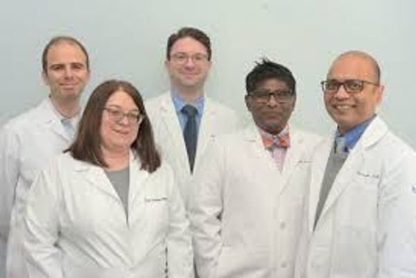 Group of five medical professionals in white lab coats posing for a photo.