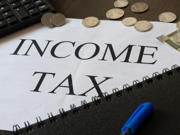 Paper titled 'INCOME TAX' with coins, pen, and calculator nearby.