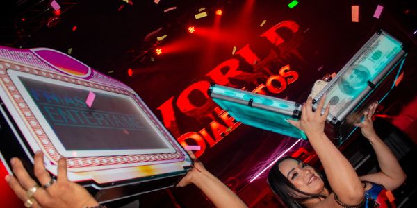 Two people holding up illuminated boxes during a lively event with red lighting and confetti.