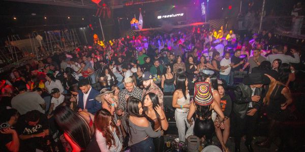 A crowded nightclub with people dancing and socializing under colorful lights.