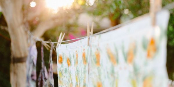Sunlit floral fabrics drying on a clothesline in a garden.