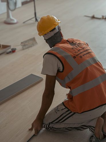 Worker laying flooring while wearing safety gear.