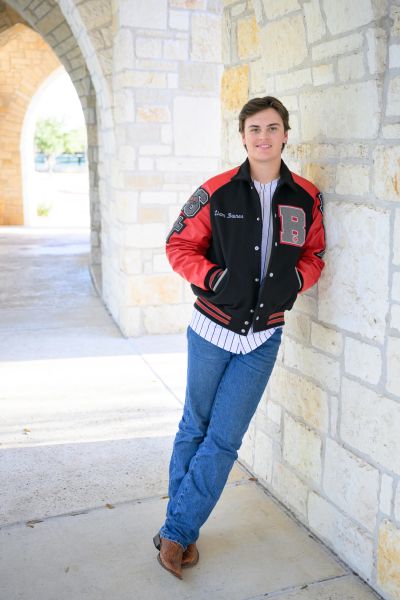 Young man leans against stone wall under archway.