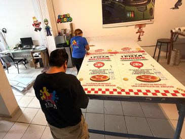 Two people working on a large printed menu in a room with Super Mario decorations.