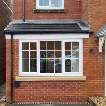 A brick house exterior with white-framed windows and a tiled roof extension.