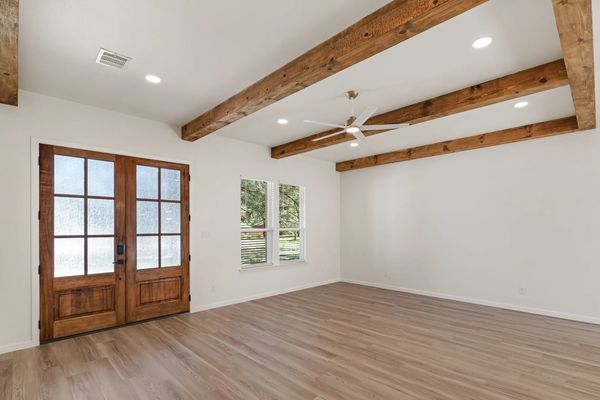 Empty room with wooden beams, double doors, and wood flooring.