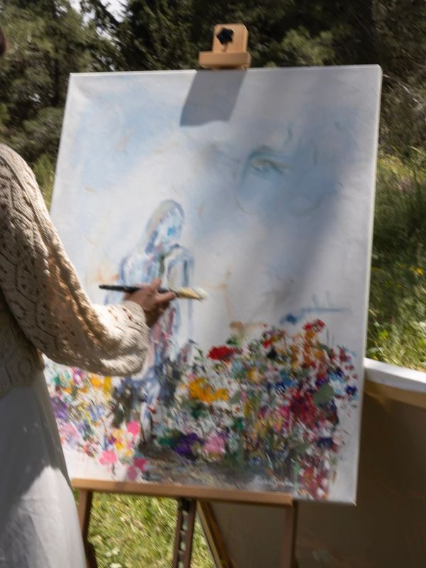 Artist painting a colorful floral scene on a canvas outdoors.