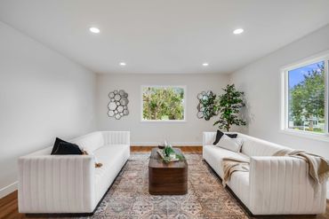 Modern living room with white sofas, wooden coffee table, and geometric wall mirrors.