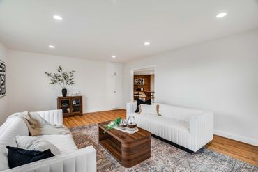 Modern living room with white sofas and wooden coffee table on patterned rug.