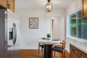 Modern kitchen nook with round table, wooden chairs, and stainless steel fridge.
