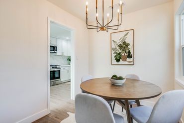 Modern dining area with a round wooden table and plant artwork.