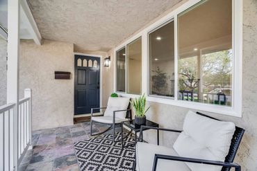 Cozy front porch with cushioned chairs and a decorative plant.