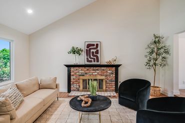Modern living room with a beige sofa, black chairs, and a brick fireplace.