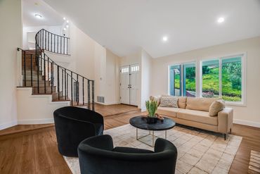 Modern living room with beige sofa, black chairs, and wooden staircase.