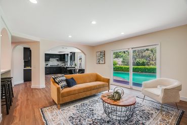 Bright living room with a mustard sofa, white chair, and pool view through sliding doors.
