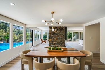 Modern dining room with wooden table and beige chairs overlooking a pool through large windows.