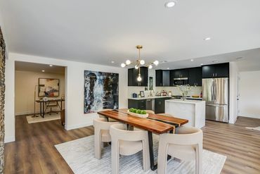Modern dining area with wooden table and beige chairs adjacent to a sleek kitchen with black cabinets.