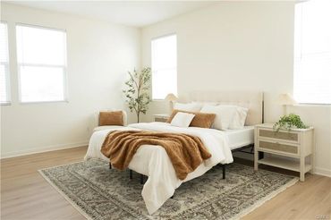 Bright bedroom with white walls, a bed with brown throw, and a patterned rug.