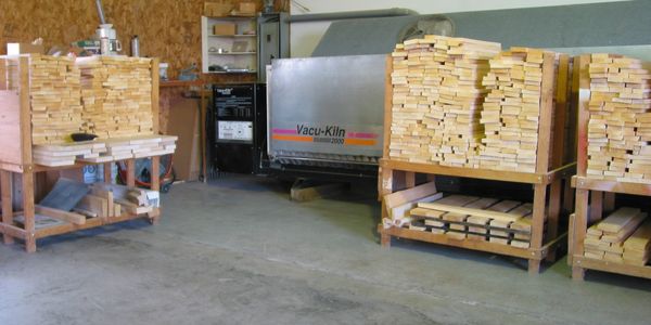 Stacks of wooden planks inside a workshop near a Vacu-Kiln dryer.
