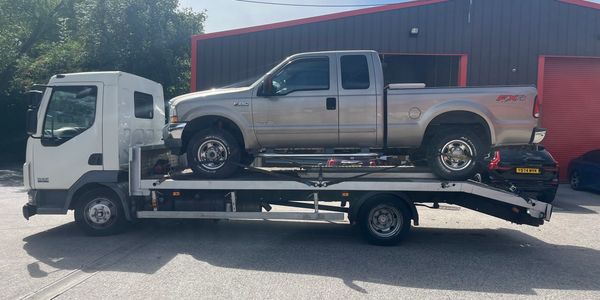Silver pickup truck on a white flatbed tow truck in a parking area.