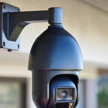 Modern black security camera mounted on a wall outdoors.