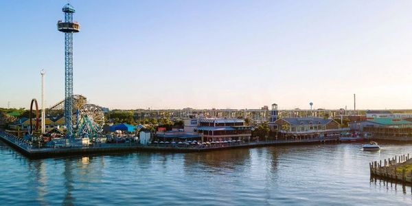 A waterfront amusement park with rides and a calm sea at sunset.