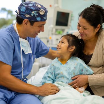 Doctor sonriente con niña y madre en hospital.