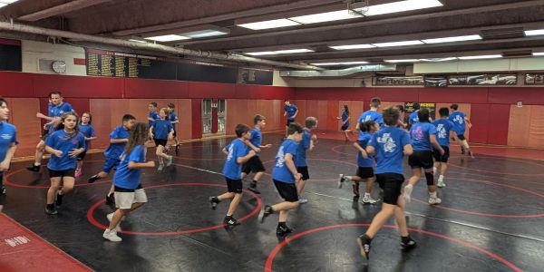 Group of kids in blue shirts running indoors.