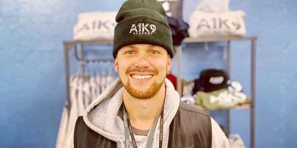 Smiling man wearing AIK Academy beanie and hoodie indoors.