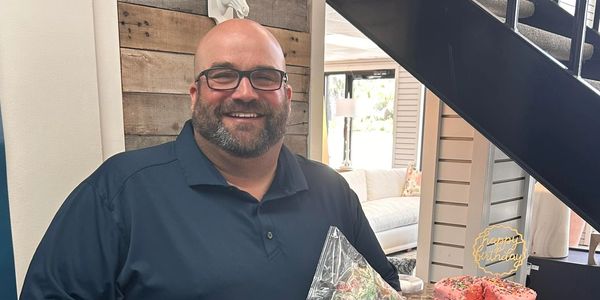 Smiling man holding pickles and candy near a birthday cake.