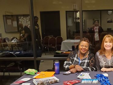 Two women smiling behind a table with brochures and giveaways.