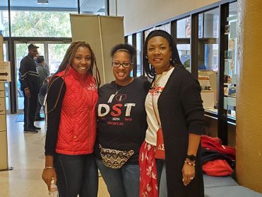 Three women smiling indoors, wearing sorority-themed attire.