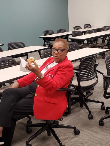 Woman in red blazer eating a treat in an empty classroom.