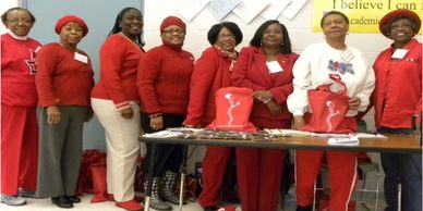Group of women dressed mostly in red standing behind a table.