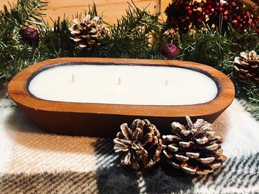 Wooden candle holder with three wicks surrounded by pine cones and festive greenery.