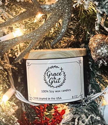 Grace & Grit soy wax candle surrounded by festive holiday decorations and lights.