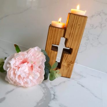 Wooden candle holder with cross cutout and pink flower on marble surface.