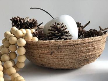 Rustic bowl with pine cones, wooden beads, and a white decorative apple.