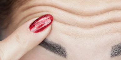 a finger with a red finger nail pointing to her creased lines on her forehead